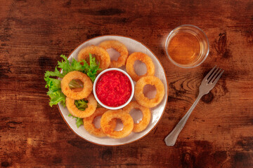 Calamari rings. Deep fried squid rings with green salad, ketchup dip and white wine, top shot on a dark rustic wooden background