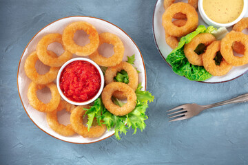 Calamari rings. Deep fried squid rings with lettuce and various sauces, overhead flat lay shot on a blue background