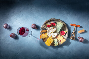 Cheese and wine tasting, overhead flat lay shot on a blue background with a place for text. Brie, blue cheese and other cheeses, with a glass of red wine