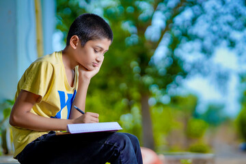 Fototapeta premium Indian school boy holding phone distance learning class using mobile application, watching online lesson, video calling in app making notes studying at home