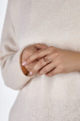 Cropped shot of a lady with laconic golden ring shaped as letter S on the middle finger. Lady in white sweater is posing with joined hands. 