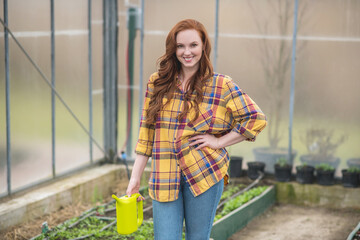 Happy woman with watering can standing in greenhouse