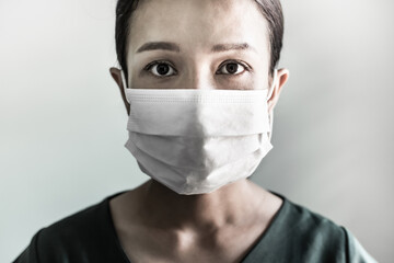 Asian woman wearing face mask against coronavirus pandemic. Studio head shot masked woman looking at the camera on grey background. Coronavirus or Covid-19 concept.