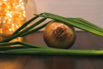 Collection of onion. Green onions lie on the head of onions on the table, close-up. Christmas lights. Ingredients and herbs for preparing a festive lunch or dinner. Fresh vegetables