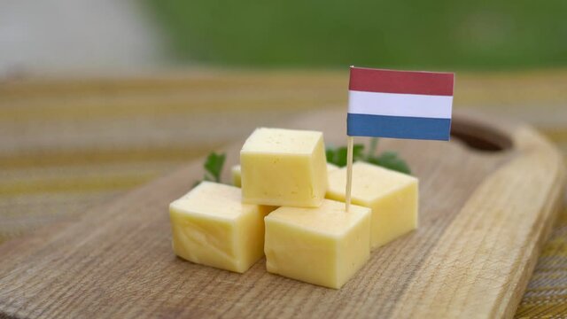 Gouda cheese cubes on wooden board with Dutch flags for party. Man's hand places toothpick with flag of the Netherlands