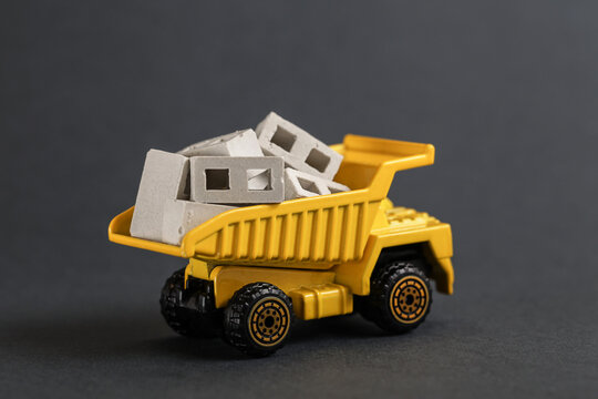 Toy dump truck delivering concrete block. Transportation construction materials on building site