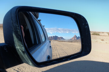Views through the rear view mirror of a car of the Spitzkoppe Mountains in Namibia on a gravel road...
