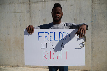 African-american man holds up a banner that reads freedom is a right. The man holds a shackle or handcuffs in his left hand. Human rights. Stop racism. Black lives matter.