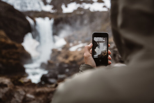 Anonymous traveler taking photo of waterfall with phone
