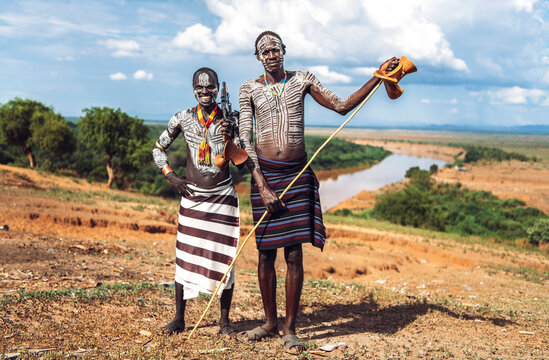 Two men with a machine gun standing near Omo river on Karo tribe