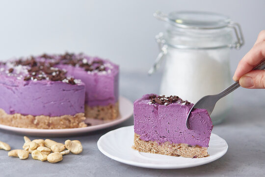 Vegan raw blueberry cake. The presence of a person without a face. The hand with the spoon breaks off a piece of cake