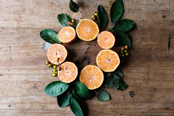 Amazing circle shaped composition of orange halves among green leaves and small berries on rustic table