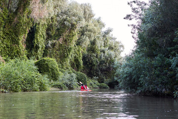 Fototapeta na wymiar Couple kayaking on river together with green trees in the backgrounds. Having fun in leisure activity. Woman and man on the kayak. Sport, relations concept.