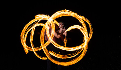 Couple of fire artists create fiery patterns spinning burning pois in night darkness outdoors, art