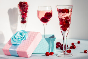 Fototapeta na wymiar set of glasses of pink gin or vodka infused with cranberry among frozen berries, a long-stemmed glass with cherry liqueur or any red alcoholic cocktail standing in gift box