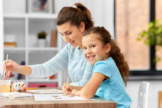 family, hobby and leisure concept - happy smiling mother spending time with her little daughter drawing or painting wooden chipboard cutouts with colors at home