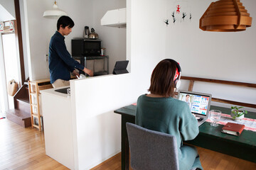 自宅で仕事をする女性と家事をする男性 © Monet