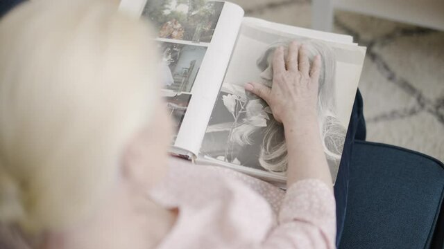 Mature woman looking at old photo of herself, remembering youth, happy memories