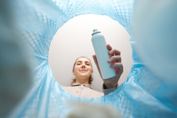 recycling, waste sorting and sustainability concept - woman throwing hair spray bottle into trash...