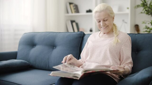 Happy mature woman looking through family album photos and smiling, memories