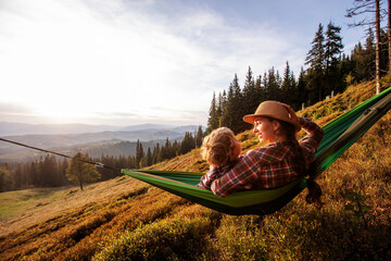 Boy with mom resting in a hammock in the mountains at sunset - 438377105