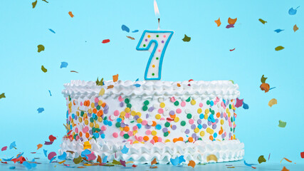 Colorful tasty birthday cake with candles shaped like the number 7. Pastel blue background.