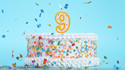 Colorful tasty birthday cake with candles shaped like the number 9. Pastel blue background.