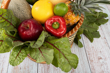 Fresh fruits and vegetables in a basket on wooden background.