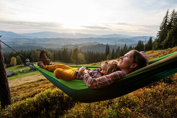 Boy with mom resting in a hammock in the mountains at sunset