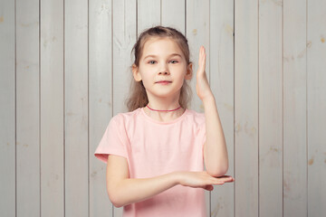 Intelligent teen girl in pink t shirt raises her hand up with a happy smile to attract attention and answer a question