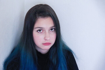 Portrait of a disgruntled upset crying teenage girl with blue hair sitting in a corner. Mental health concept.