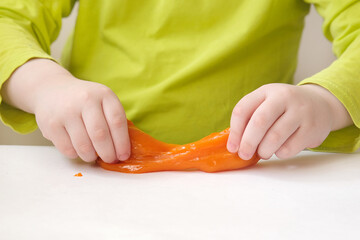 close-up of childrens hands stretching orange slime on a white table. The concept is the development of fine motor skills and tactile sensations in children. Horizontal photo.