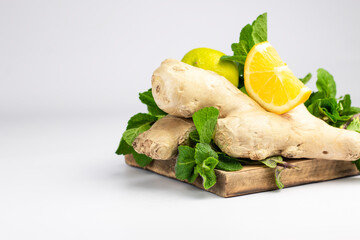 Ginger root, green fresh mint and lemons on wooden tray.