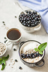 Oatmeal with blueberries, sunflower seeds and coconut for breakfast, decorated with a sprig of mint and a cup of coffee. Close-up of porridge, rest in soft focus
