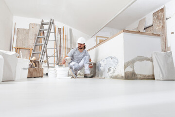 plasterer man at work, take the mortar from the bucket with trowel to plastering the wall of interior construction house site and wear helmet, panoramic image