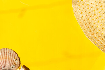Part of a straw hat and seashells on a yellow surface on a sunny day. Summertime vibes concept....