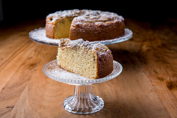 Apple pie on a glass stand. Brown wood background. Powdered sugar  