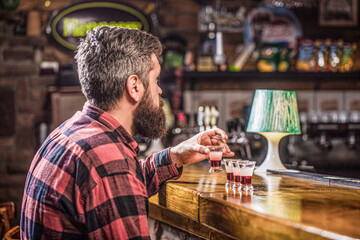 Drinking alcohol into shot glasses in a nightclub or bar. Bearded man shots cocktail. Tequila...