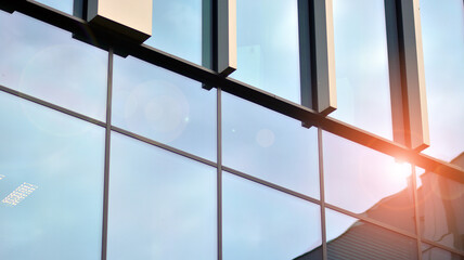 Facade texture of a glass mirrored office building. Fragment of the facade. Bottom view of modern skyscrapers in business district in evening light at sunset with lens flare filter effect.