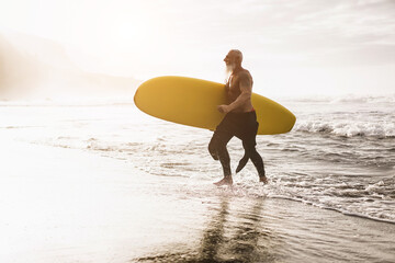 Senior surfer man walking on the beach after surf session at summer sunset - Focus on face
