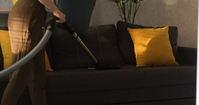 Girl vacuums the sofa. Cleaning couch from the dust. Housewife cleans the house. Cleaning service.