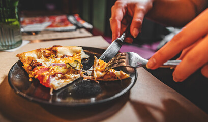 woman hands with knife and fork cutting pizza on table in cafe