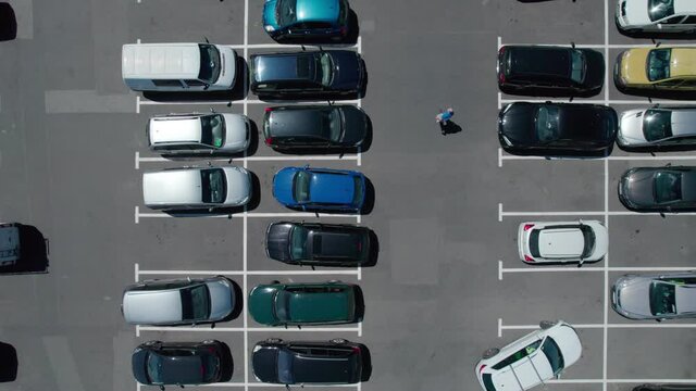 Cars in the parking lot in the air view. People move, cars park and go, shopping frenzy.
