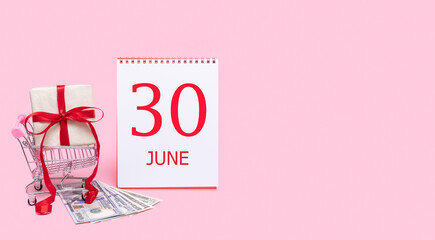 A gift box in a shopping trolley, dollars and a calendar with the date of 30 june on a pink background.