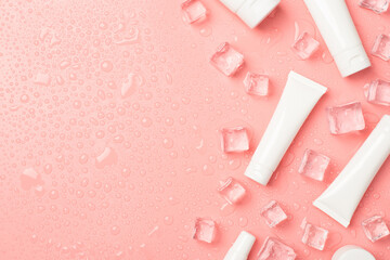 Top view photo of several different sizes white tubes without label ice cubes on the right and drops on isolated pastel pink background with blank space on the left