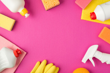 Top view photo of sponges viscose rags rubber gloves and white detergent bottles on isolated pink background with copyspace in the middle