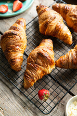 Freshly baked croissants on cooling rack on wooden table.