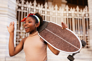 Portrait of happy african-american woman with skateboard. Young stylish woman with skateboard outdoors.