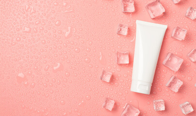 Top view photo of white cream bottle without label ice cubes on the right and drops on isolated pastel pink background with copyspace on the left