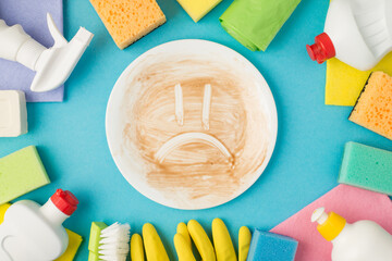 Above photo of equipment for cleaning and dirty plate with sad smile picture in the middle isolated on the blue background